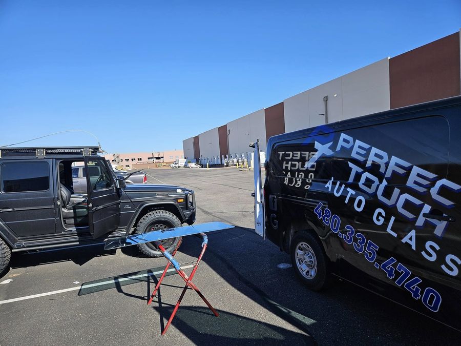 A windshield ready for installation beside the Perfect Touch van at a customer's workplace